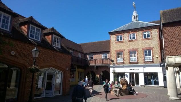 shops, cobbled streets, people walking around. Lion statue to the right.