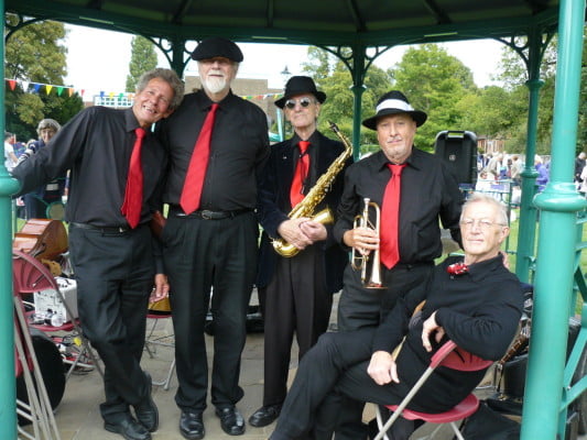 5 Males smartly dressed in the bandstand. 2 holding instruments.