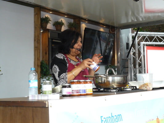 female with microphone performing a cooking demo.