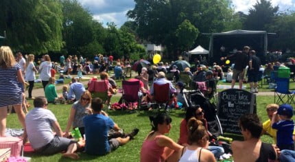 Crowd of people in park, with stage and bunting