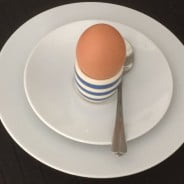 Egg in blue and white egg cup on white plate.