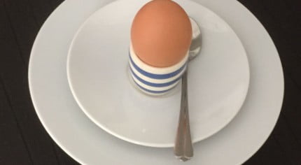 Egg in blue and white egg cup on white plate.