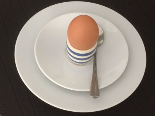 Egg in blue and white egg cup on white plate.