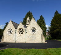 White stone chapel, tarmac driveway around, trees in the background.