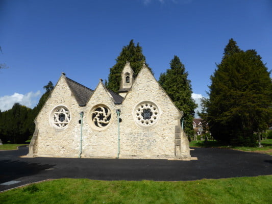 White stone chapel, tarmac driveway around, trees in the background.
