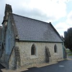 exterior of white stone chapel, trees to the right.