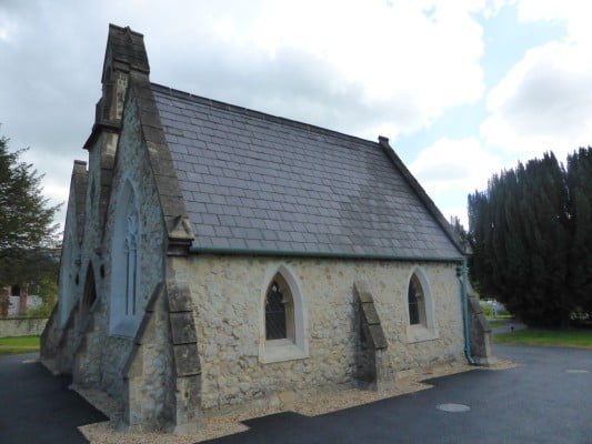 exterior of white stone chapel, trees to the right.