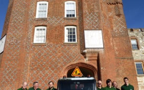 group of males next to a floral van, red brick castle behind.