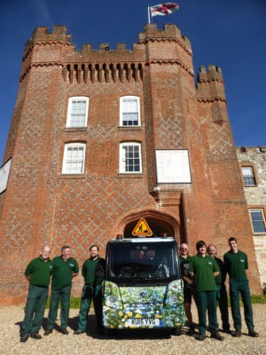 group of males next to a floral van, red brick castle behind.