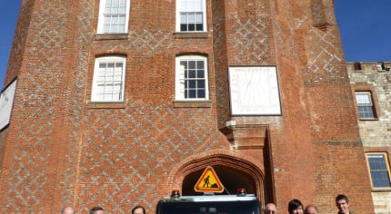 group of males next to a floral van, red brick castle behind.