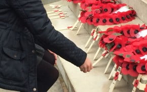 Girl lays wooden cross on war memorial.