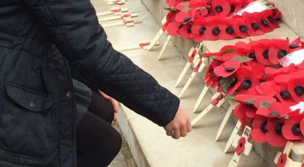 Girl lays wooden cross on war memorial.