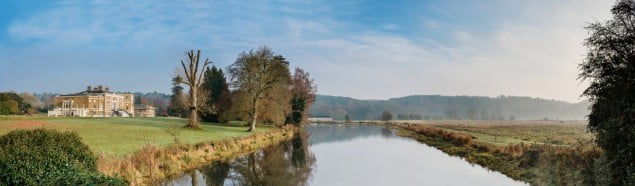 River and expanse of grass in front of grand old house. Blue sky and trees