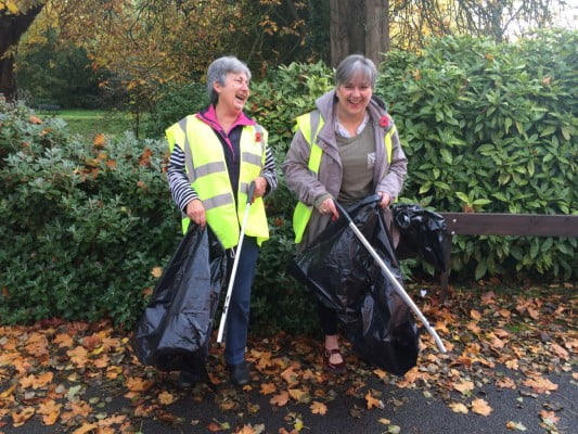 Two females in high viz jackets holding black sacks and litter pickers.