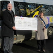 Man and Mayor stand to the side of a community bus holding large cheque