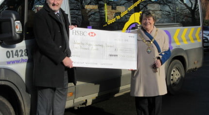 Man and Mayor stand to the side of a community bus holding large cheque