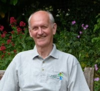 Smiling man sitting in front of flower bed. Member of Bourne Conservation Group