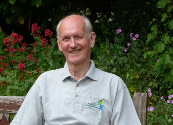 Smiling man sitting in front of flower bed. Member of Bourne Conservation Group