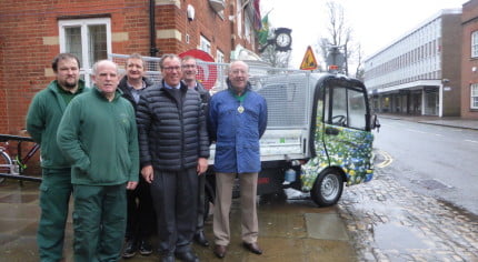 Six men in front of electric vehicle.