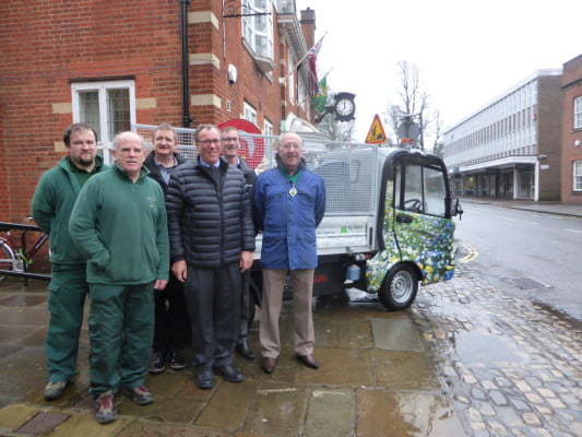 Six men in front of electric vehicle.