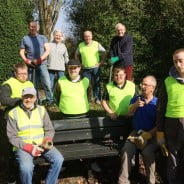 Nine males and one female sitting on a bench or standing behind wearing hi res clothing and gardening gloves