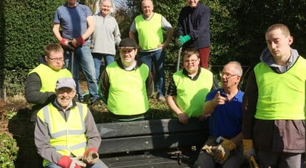 Nine males and one female sitting on a bench or standing behind wearing hi res clothing and gardening gloves