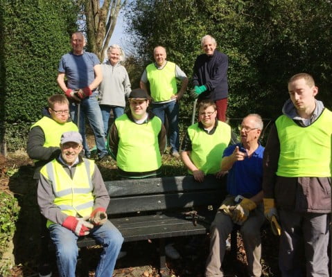 Nine males and one female sitting on a bench or standing behind wearing hi res clothing and gardening gloves