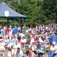 Crowd of people in park. Bandstand behind.