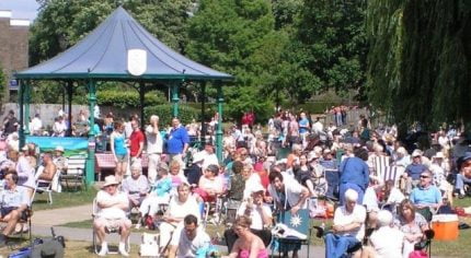 Crowd of people in park. Bandstand behind.