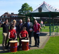 Four males and one female standing behind two children with drums