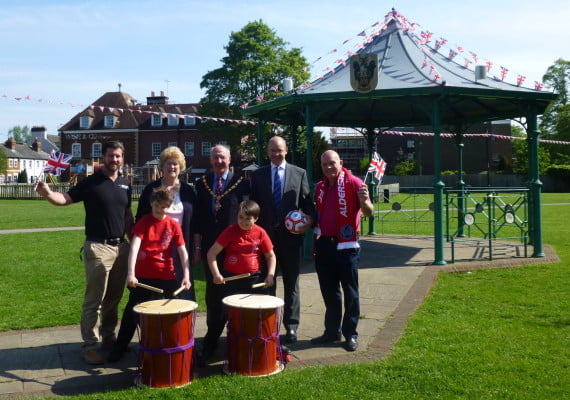 Four males and one female standing behind two children with drums