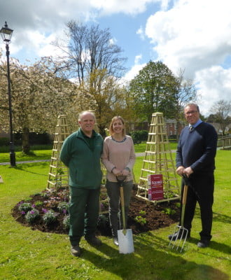 Two males and one female standing in front of flower bed