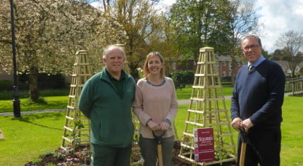 Two males and one female standing in front of flower bed