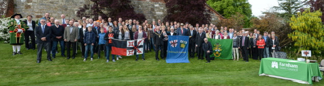 A crowd of people infront of a castle wall some holding flags