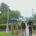 Four males standing in the park with umbrellas.