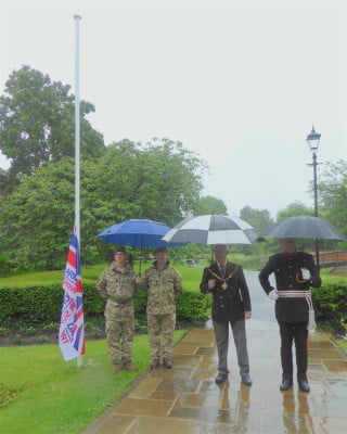 Four males standing in the park with umbrellas.