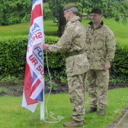 Two males attaching flag to flag pole in park.