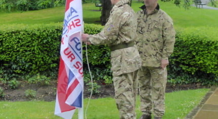 Two males attaching flag to flag pole in park.