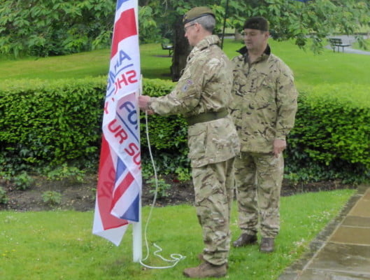 Two males attaching flag to flag pole in park.