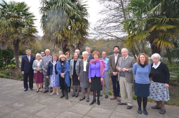 A group of adults standing in front of a flowerbed with trees behind.