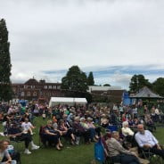 Groups of people sitting on chairs in the park watching a band.