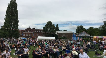 Groups of people sitting on chairs in the park watching a band.