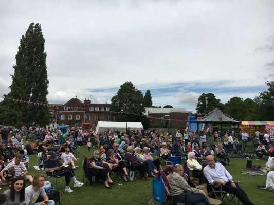 Groups of people sitting on chairs in the park watching a band.