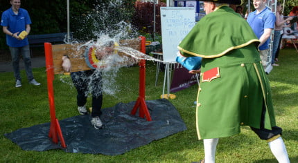 Male in stocks while male throws an bucket of water at him