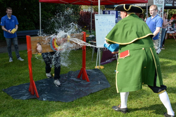 Male in stocks while male throws an bucket of water at him