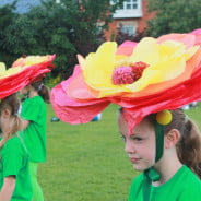 Children performers with green costumes and large flower hats .