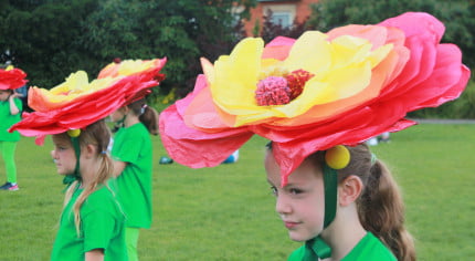 Children performers with green costumes and large flower hats .