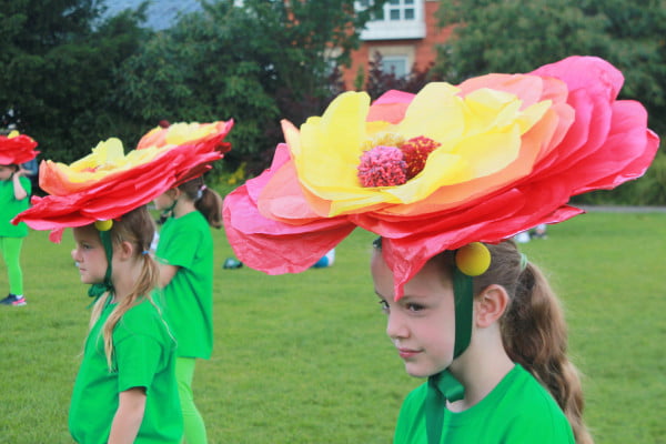 Children performers with green costumes and large flower hats .
