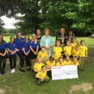 A group of adults and children with a large cheque stood in a park.