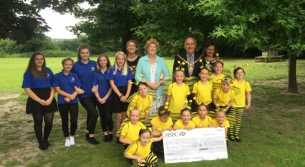 A group of adults and children with a large cheque stood in a park.